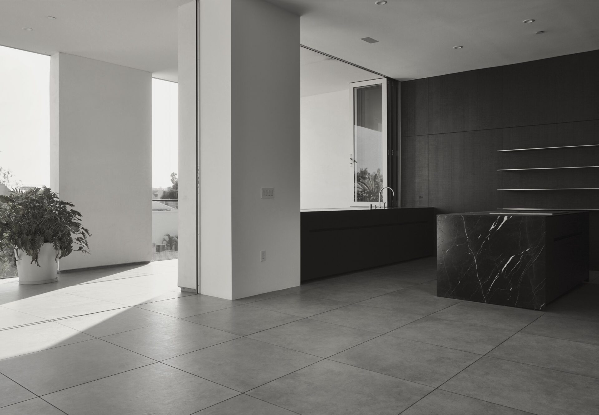 Minimalist kitchen with black marble island and dark cabinetry, adjacent to flush terrace bathed in natural light.