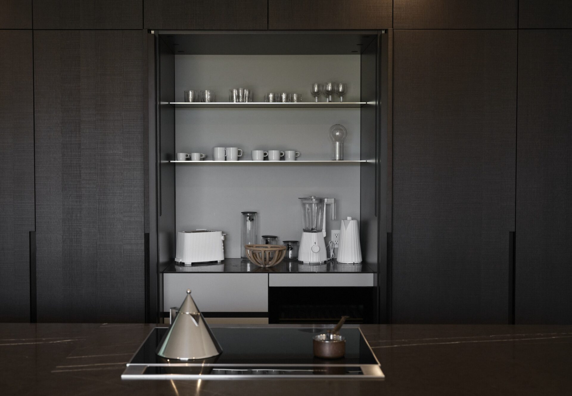 Minimalist kitchen cabinet with open shelves displaying white dishware, blender, toaster, and coffee maker.