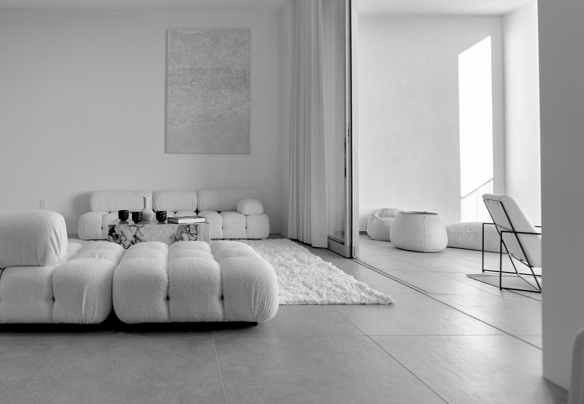 Penthouse living room featuring modular tufted seating, plush rug, and floor-to-ceiling sliding doors leading to a minimalist private terrace.