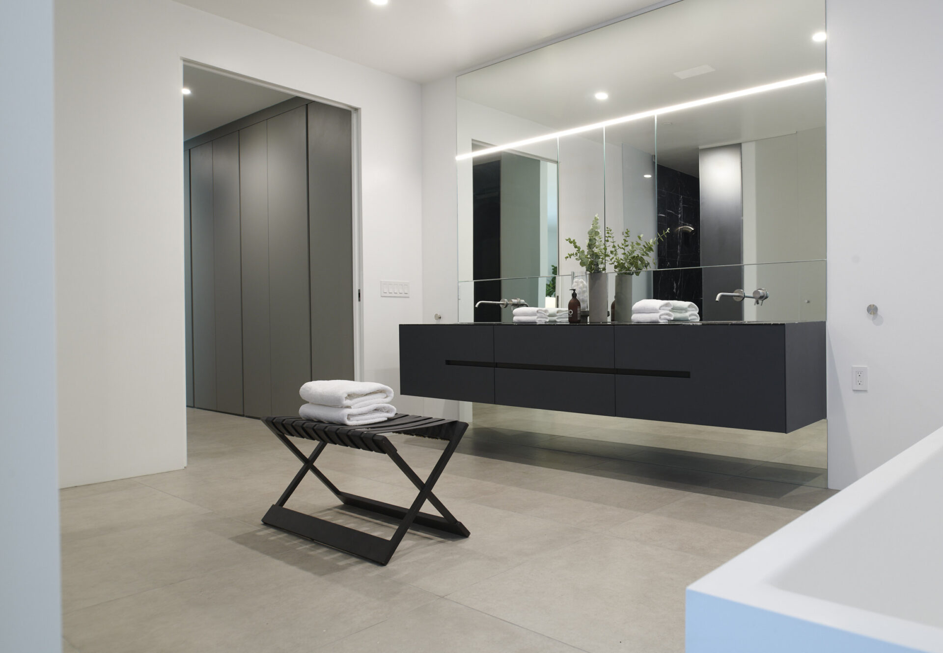Bright en suite bathroom with floating dual-sink vanity, mirrored cabinets, and towel bench near the freestanding tub.