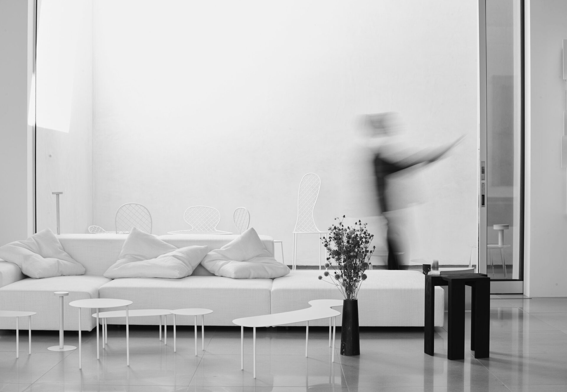 Modern West Hollywood penthouse living room with a white sofa and sculptural coffee tables, as a blurred figure opens floor-to-ceiling sliding doors to the private courtyard.
