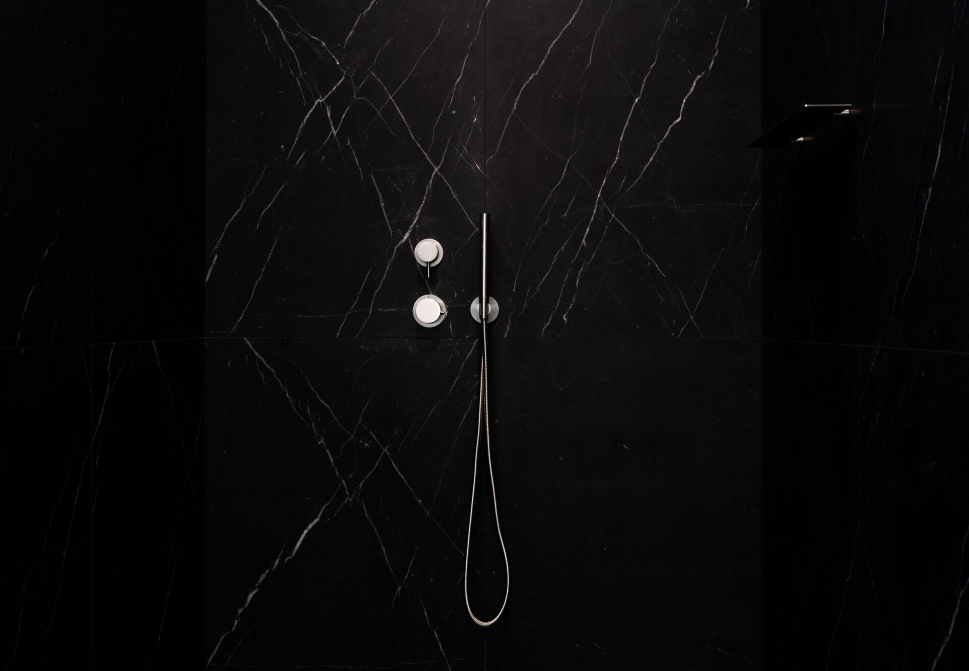 Sleek shower with black marble slab walls and minimalist chrome fixtures.