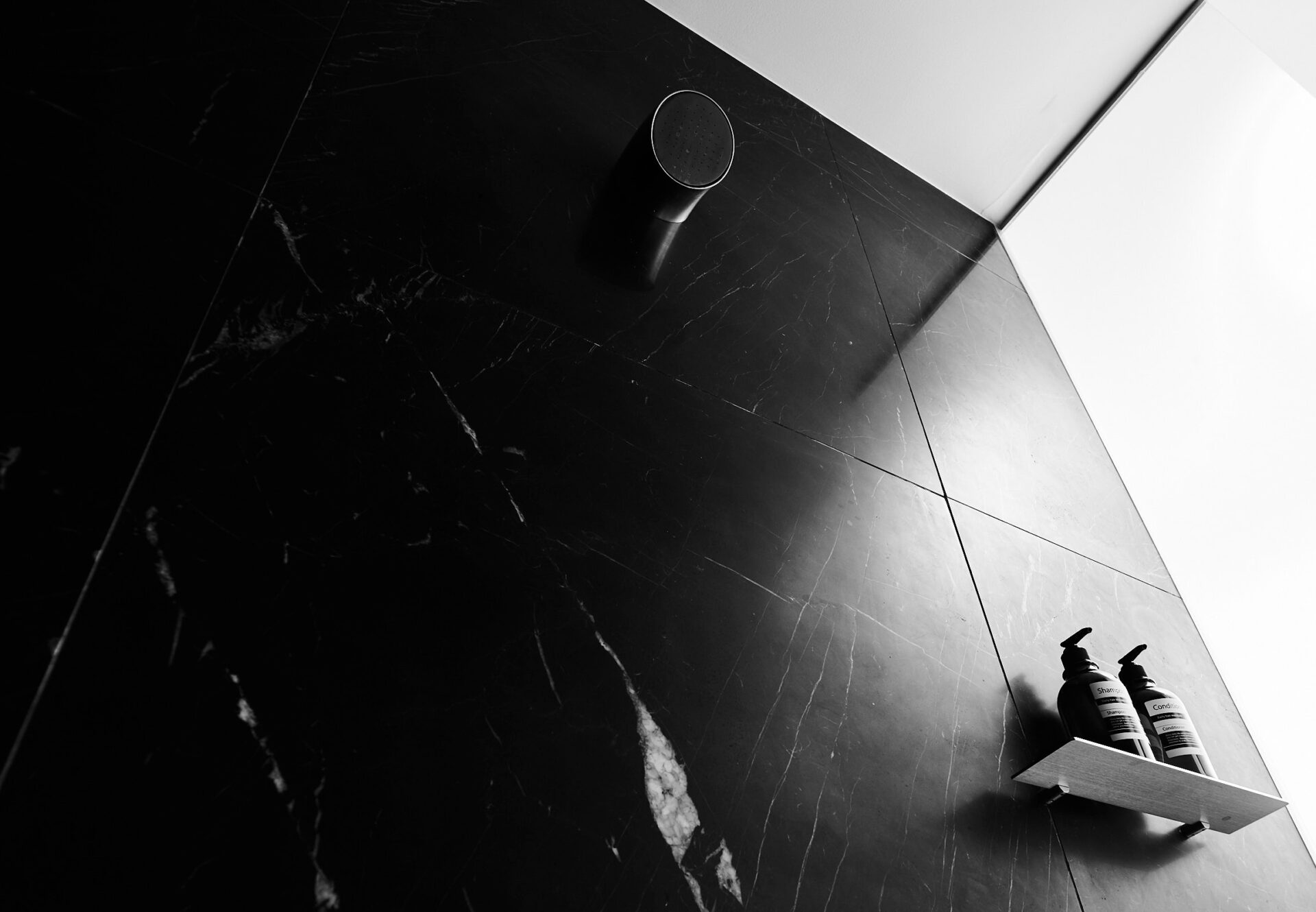 Dimly lit black marble shower with built-in shelf and wall-mounted showerhead.