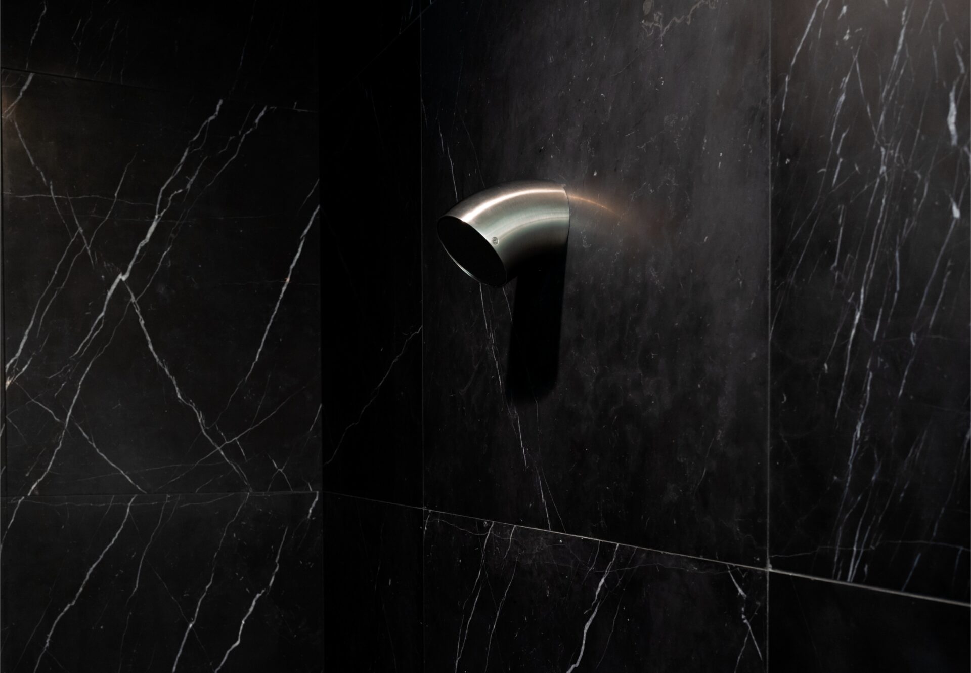 Dimly lit shower with black marble walls and a wall-mounted showerhead in a luxury West Hollywood residence.