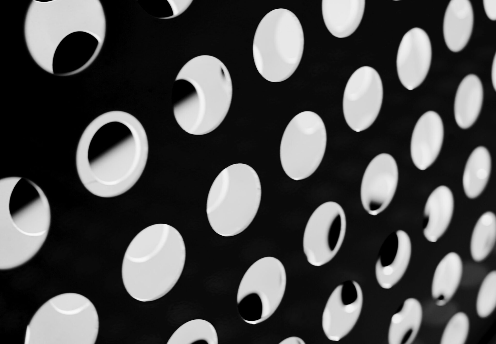 Close-up of black perforated metal panel with circular holes and visible background shapes through openings.