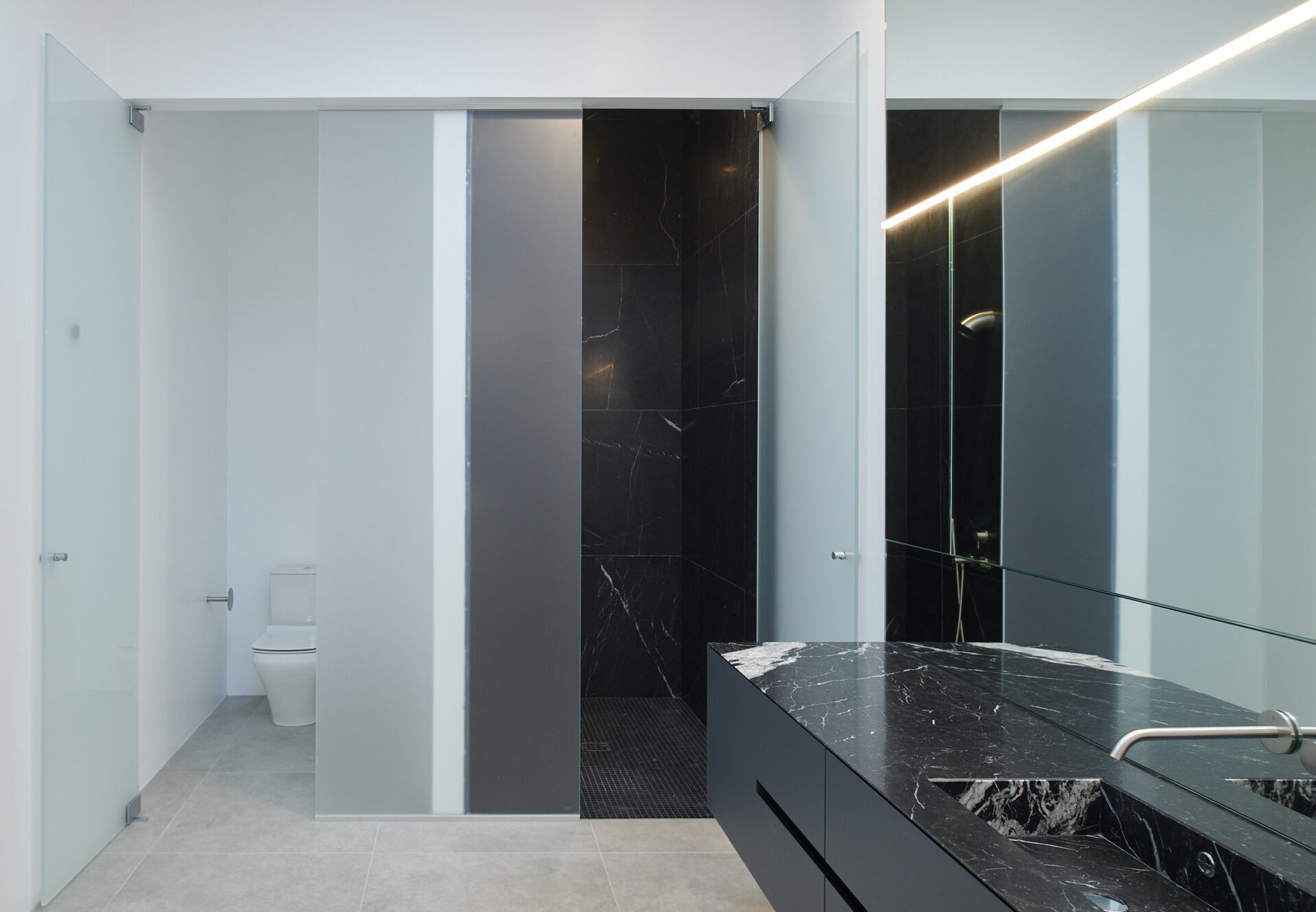 Bright bathroom with black marble vanity, wall-mounted faucet, and frosted glass doors.