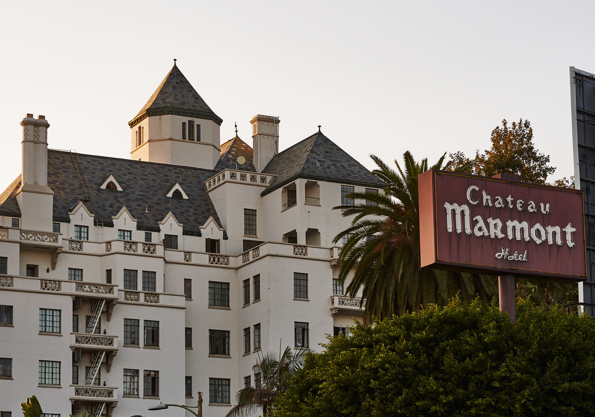 Exterior view of Chateau Marmont hotel with distinctive turrets, white facade, and surrounding palm trees at sunset.