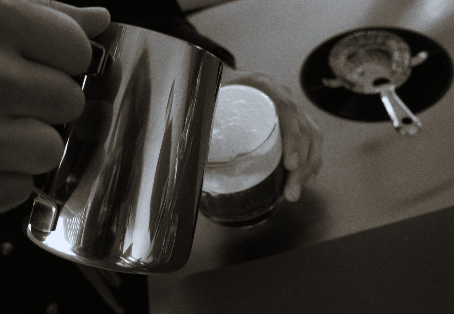 Close-up of a hand pouring steamed milk into a coffee glass at a stainless steel station, showcasing on-site amenities.