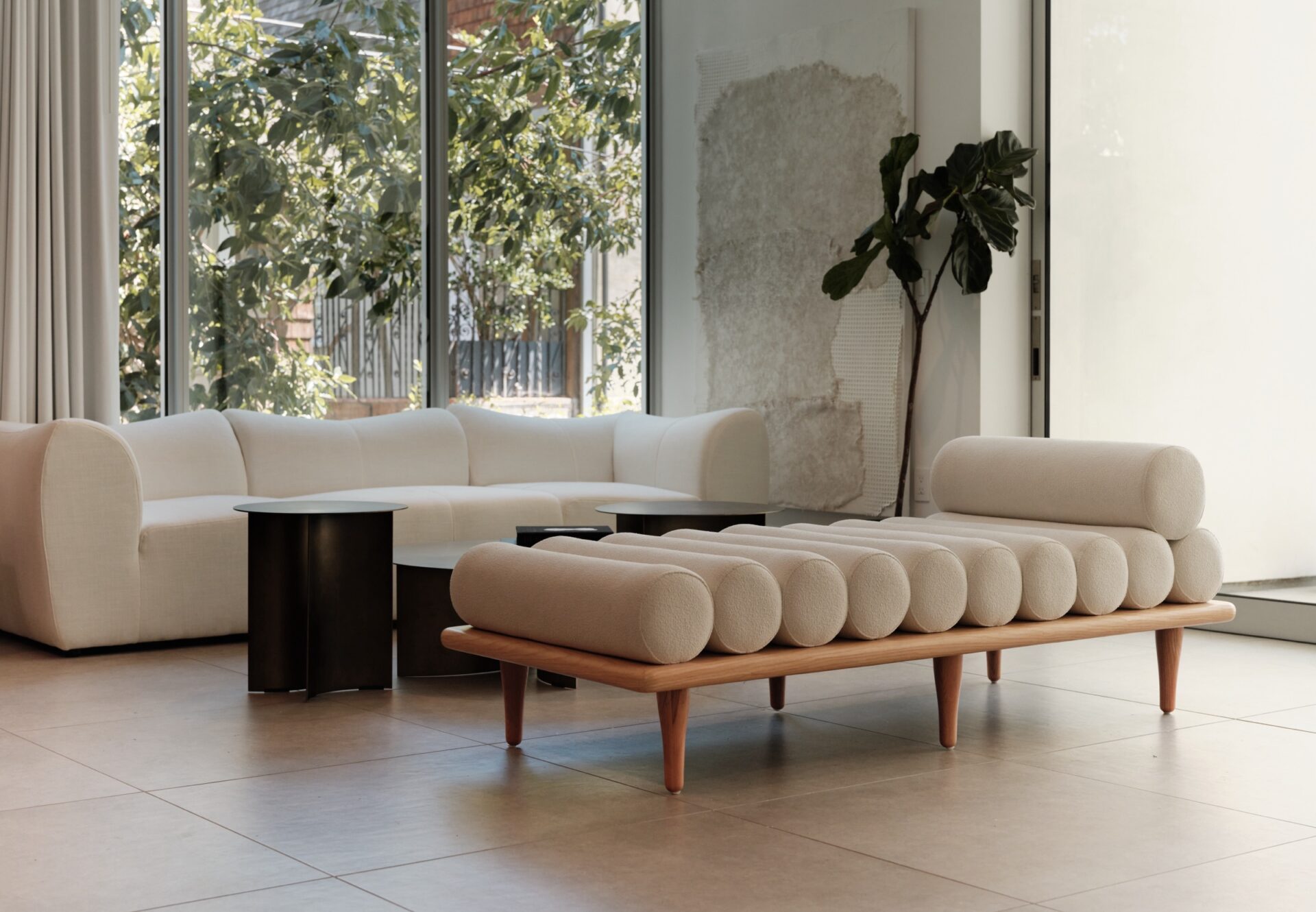 Corner one-bedroom residence with sculptural daybed, curved cream sofa, and floor-to-ceiling windows framing lush greenery.