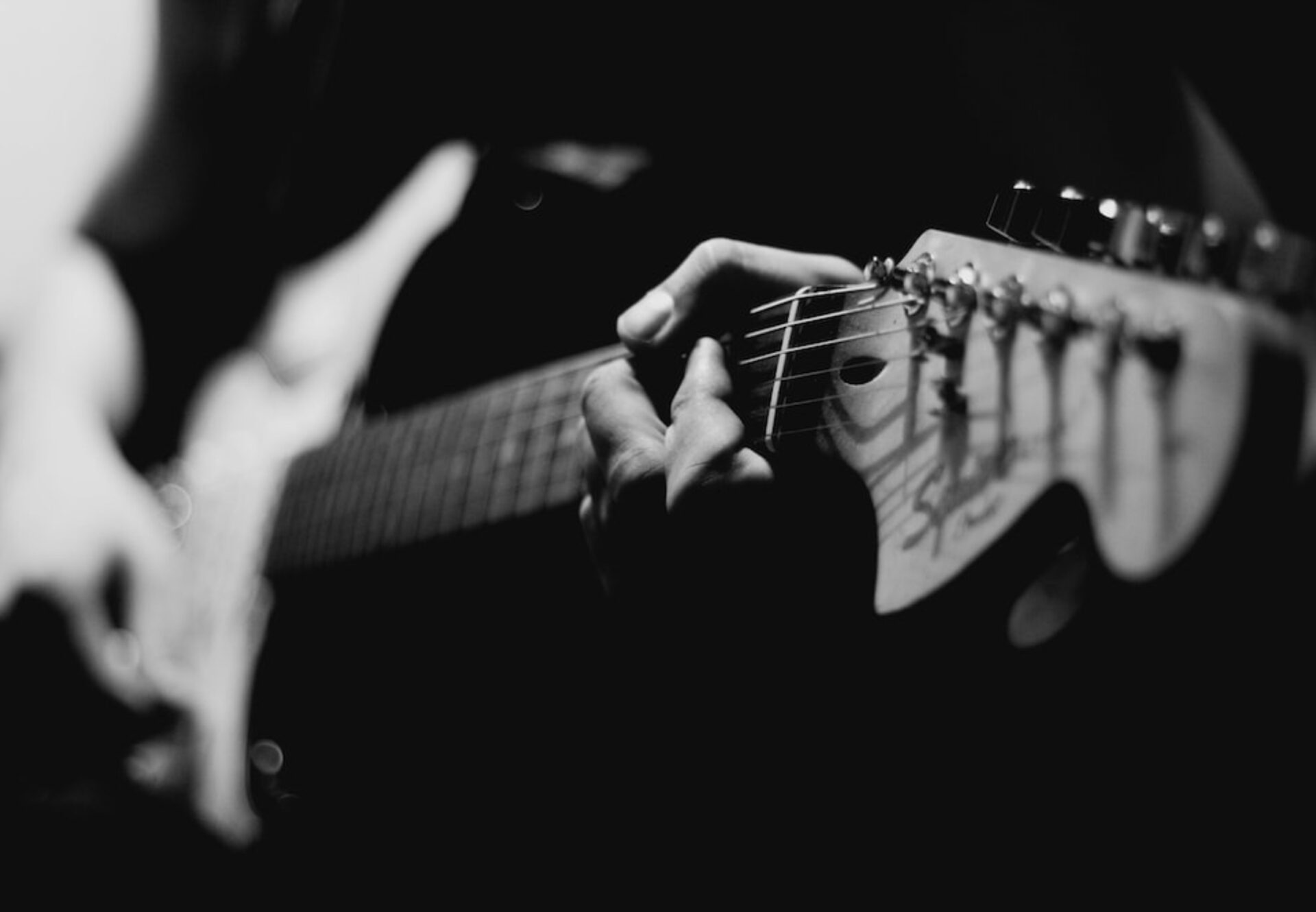 Close-up of electric guitar being played during a live music set at an evening resident event, captured in black and white.