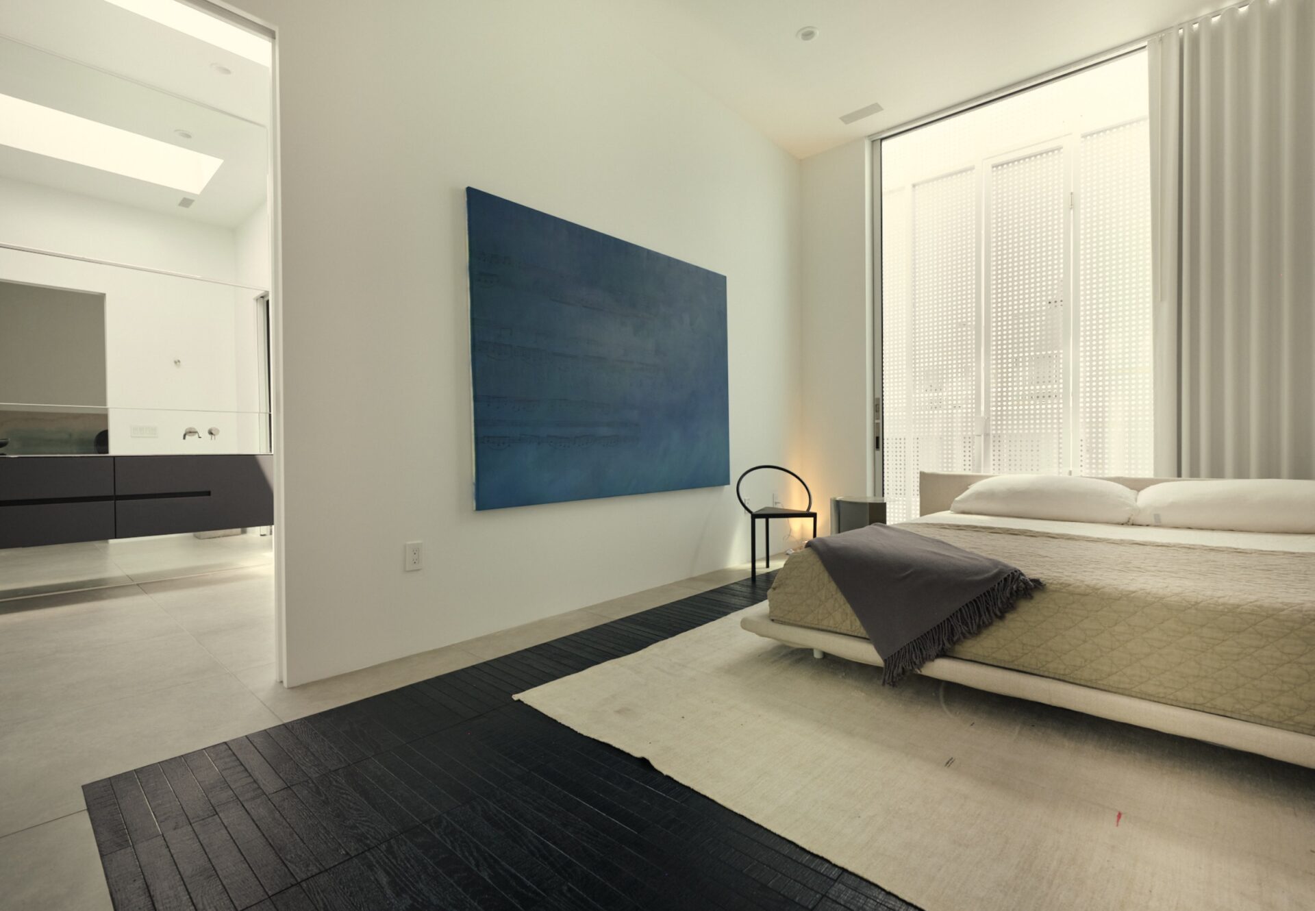 Expansive bedroom with tall ceilings, floor-to-ceiling window, blue wall art, and a glimpse into the en suite bath.
