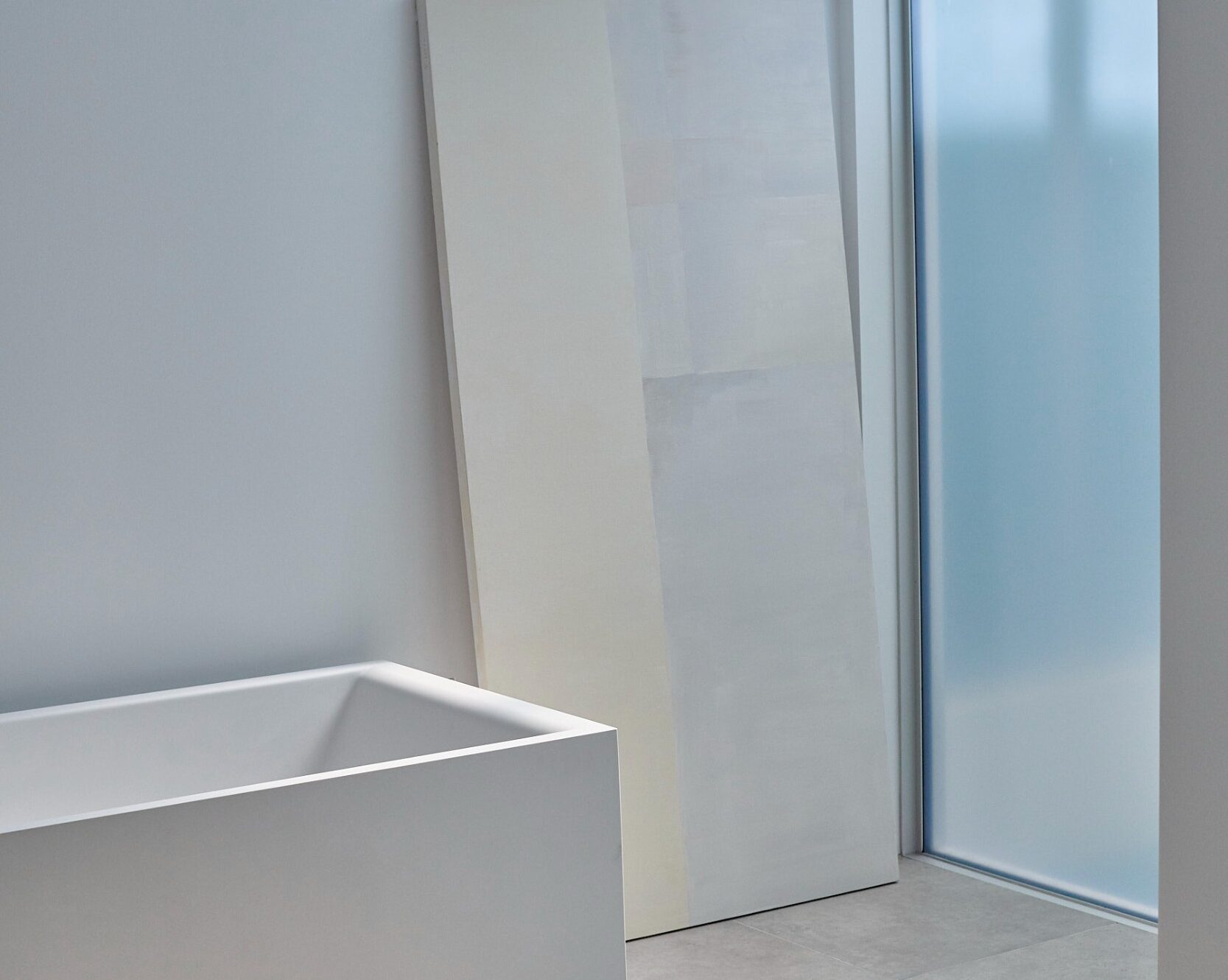 Freestanding tub under soft lighting from adjacent sunlit atrium, with leaning artwork.