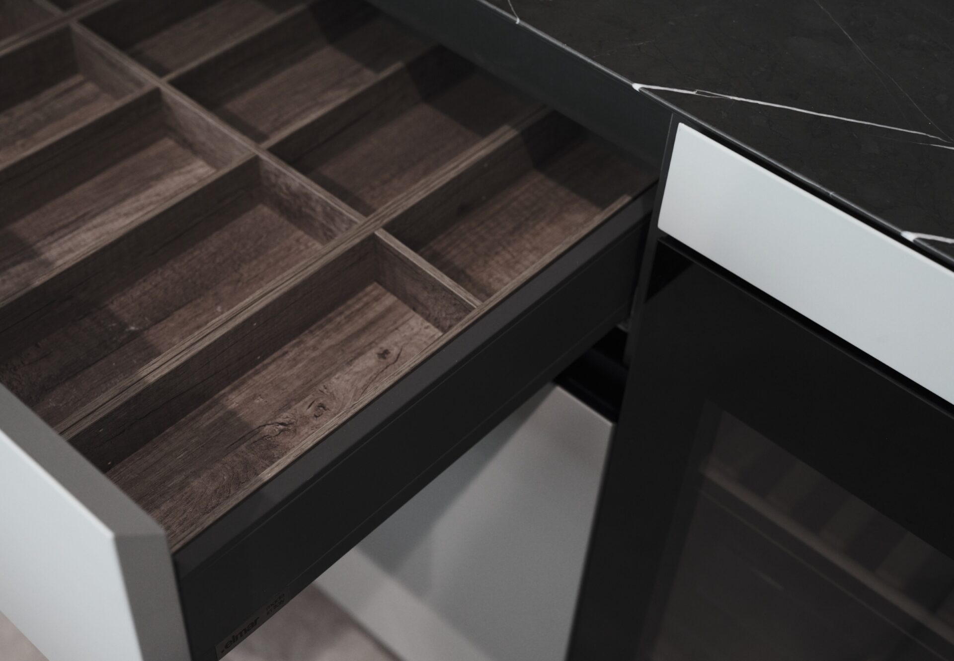 Close-up of dark wood kitchen drawer with built-in utensil dividers beneath a marble countertop and white cabinetry.