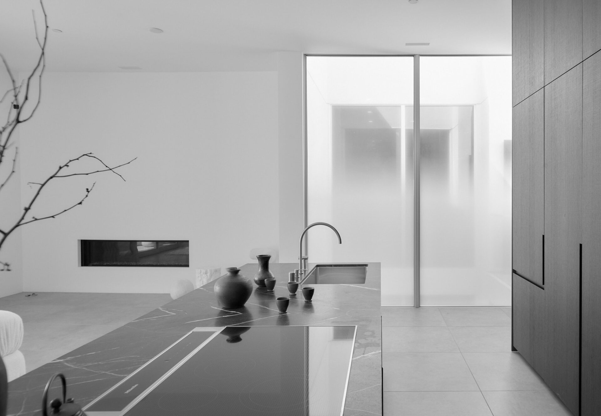 Marble kitchen island with integrated stove, facing sunlit atrium with gradient frosted glass panels in a one-bedroom residence.