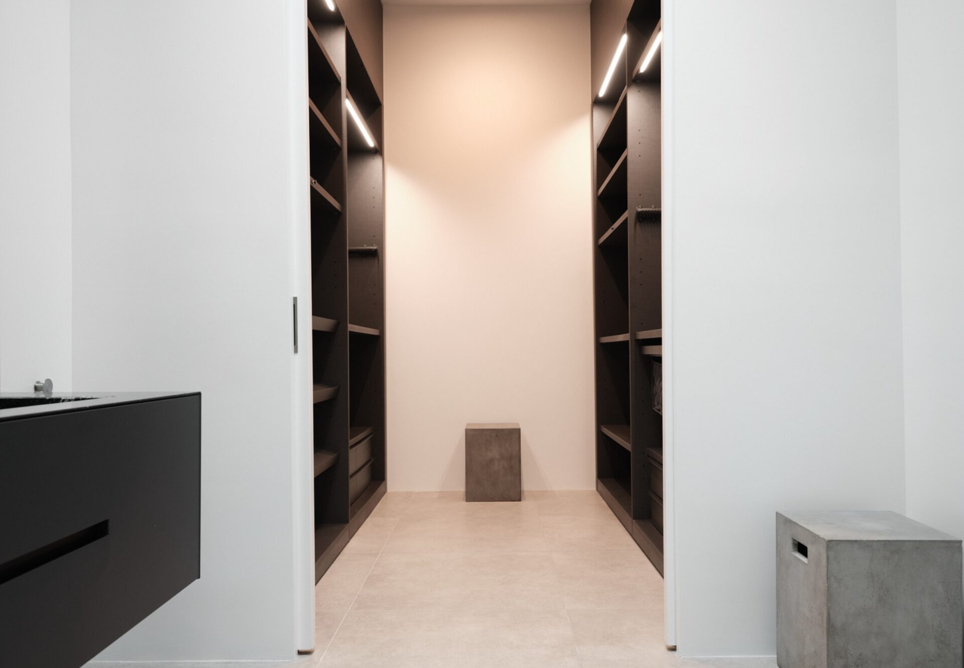 Large walk-in closet with dark wood built-in shelving, under-shelf lighting, and a side view of a floating vanity sink.