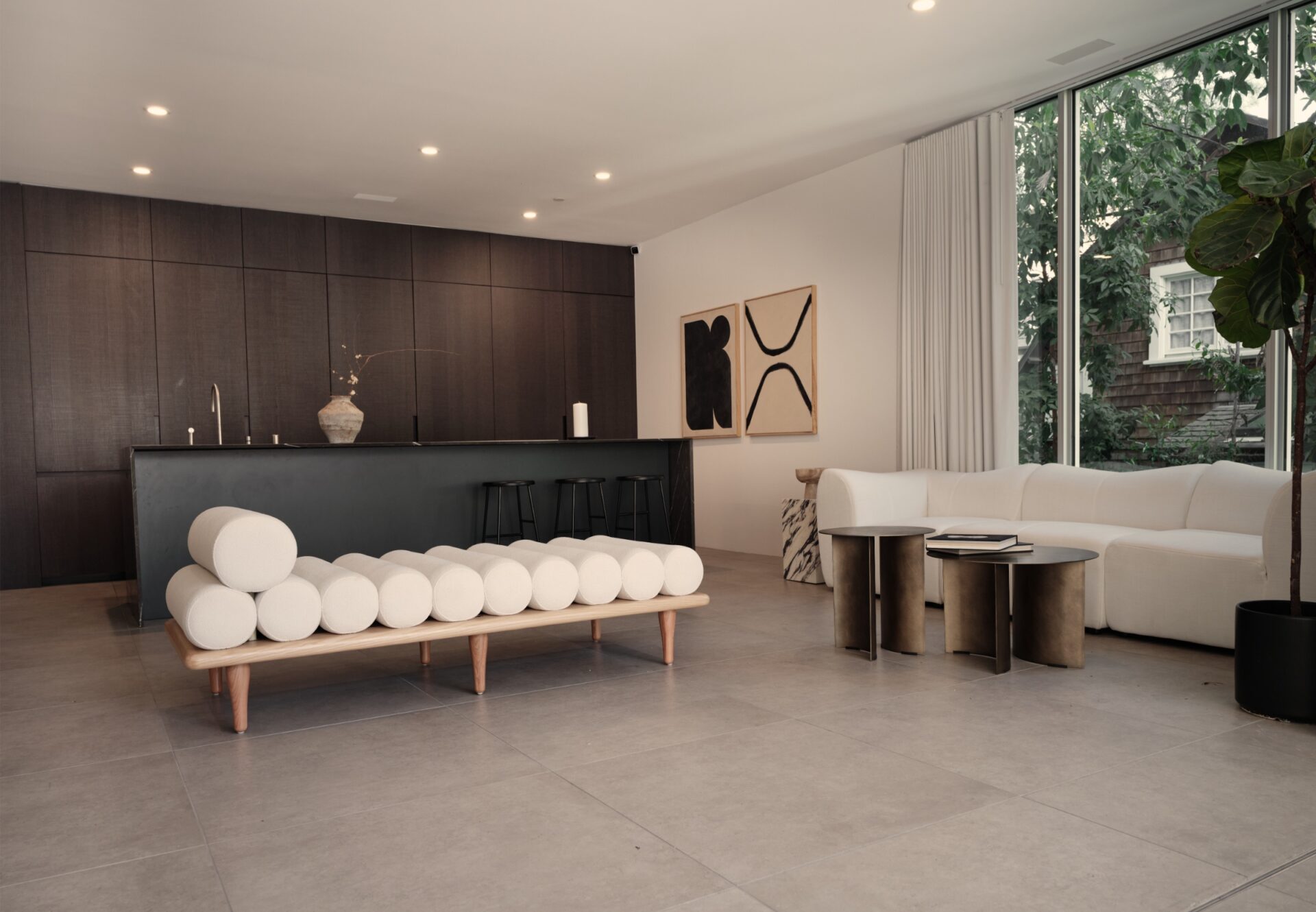 East corner one-bedroom unit with daybed, dark wood kitchen, and floor-to-ceiling windows overlooking greenery.
