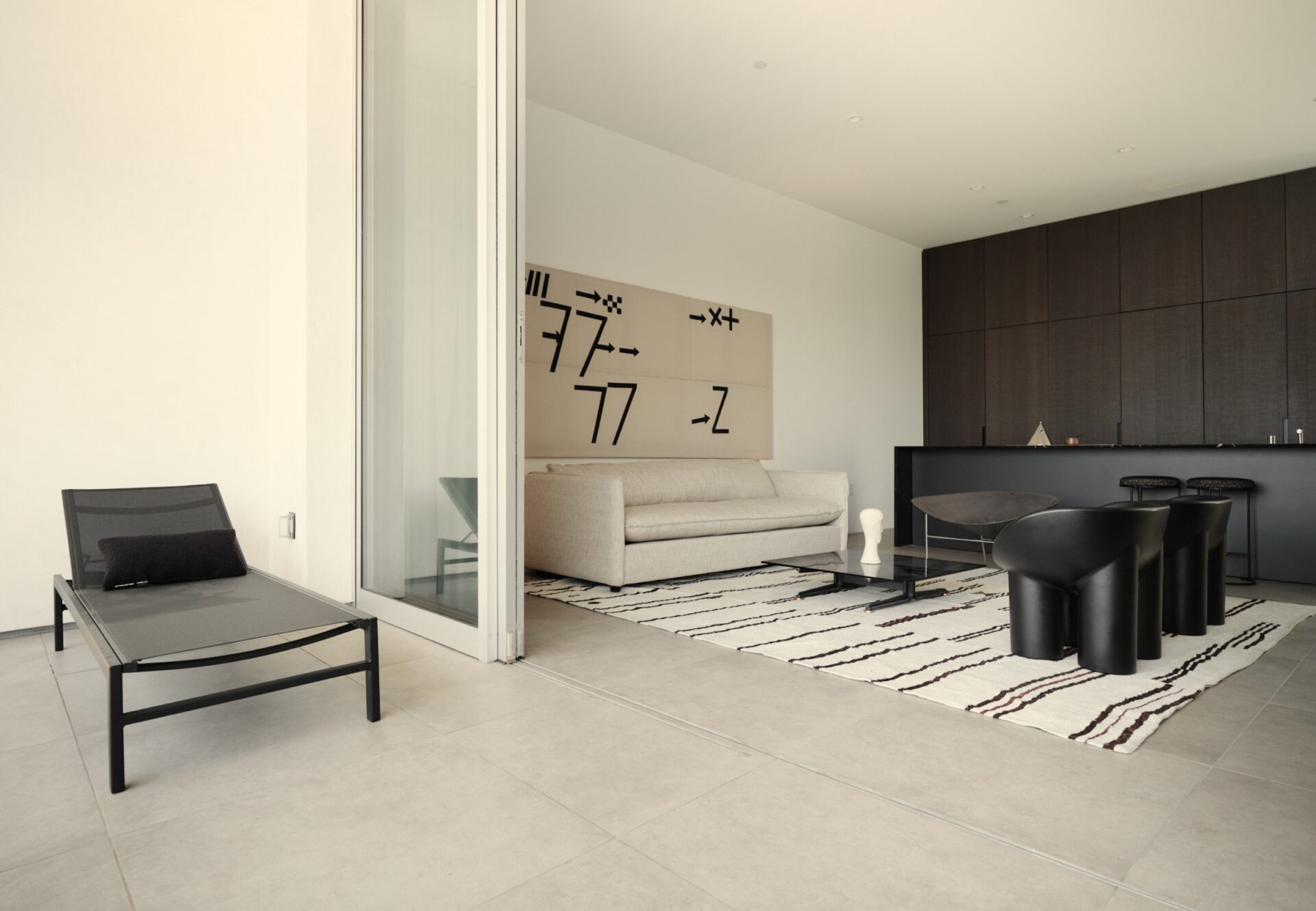 View from private terrace into a luxury penthouse one-bedroom, showcasing minimalist interiors, dark oak wood kitchen, and contemporary lounge design.
