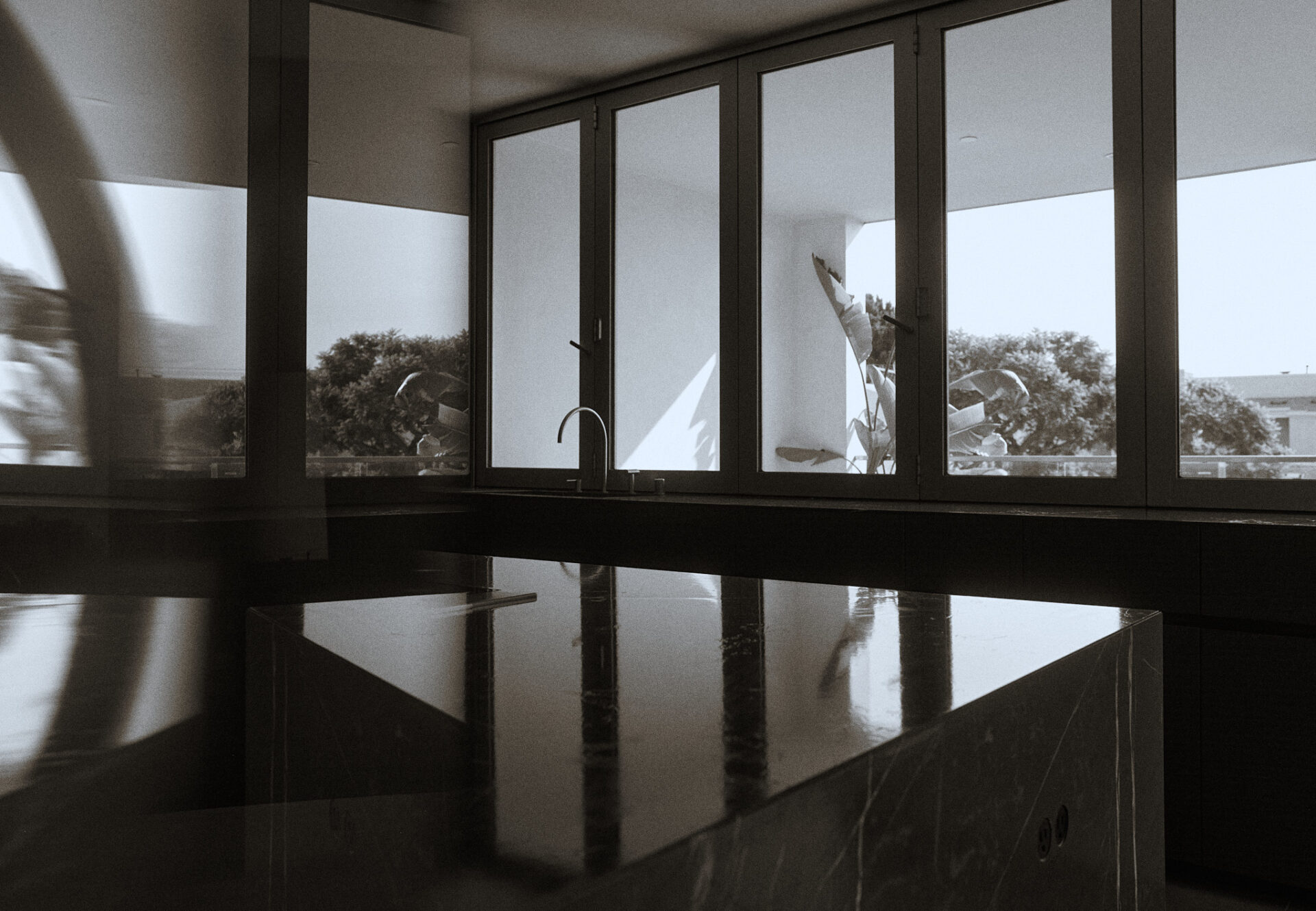 Reflective marble kitchen island with views through accordion windows revealing lush greenery and clean architectural lines.