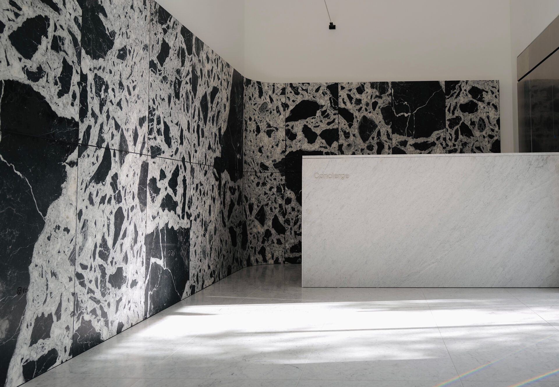 Modern luxury lobby with dramatic black-and-white marble walls, white marble concierge desk, and Carrara white marble flooring.