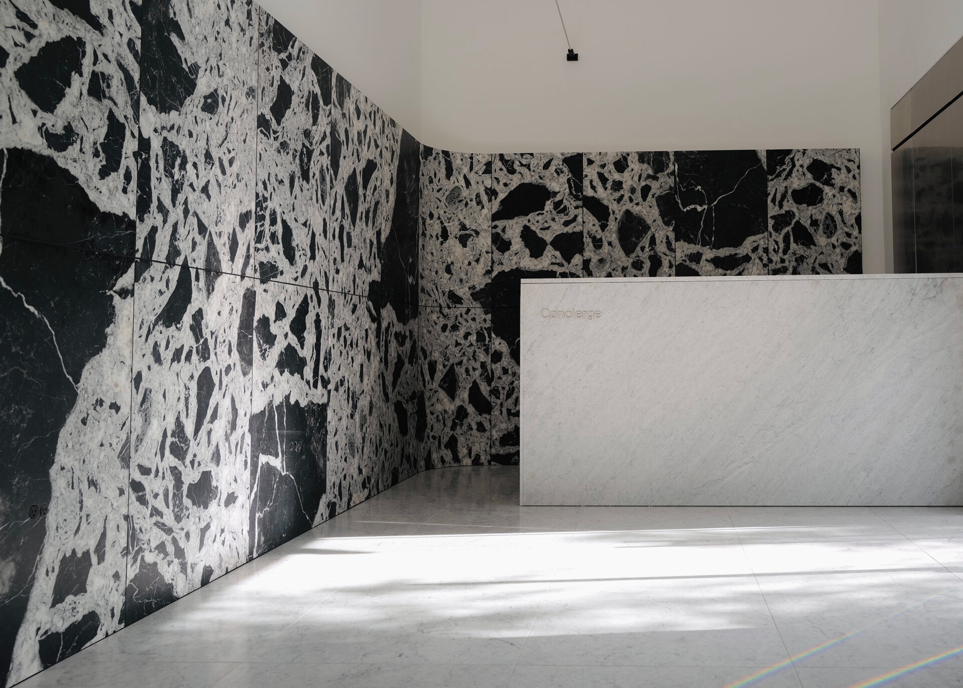 Modern luxury lobby with dramatic black-and-white marble walls, white marble concierge desk, and Carrara white marble flooring.