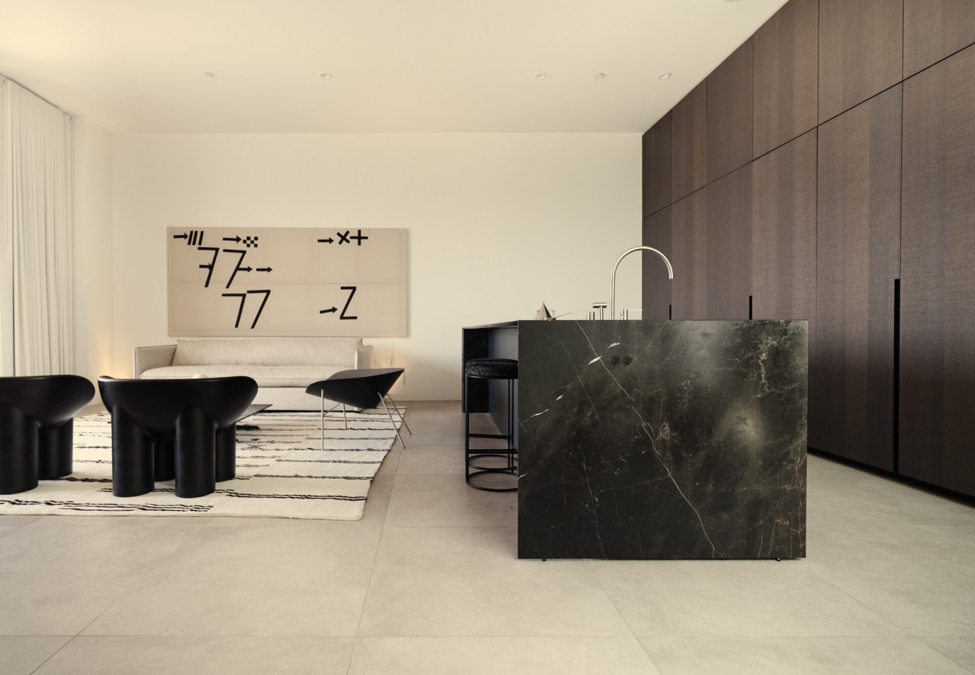 Open-concept living and kitchen area with tall ceilings, dark oak cabinetry, black marble island, and modern designer furnishings.