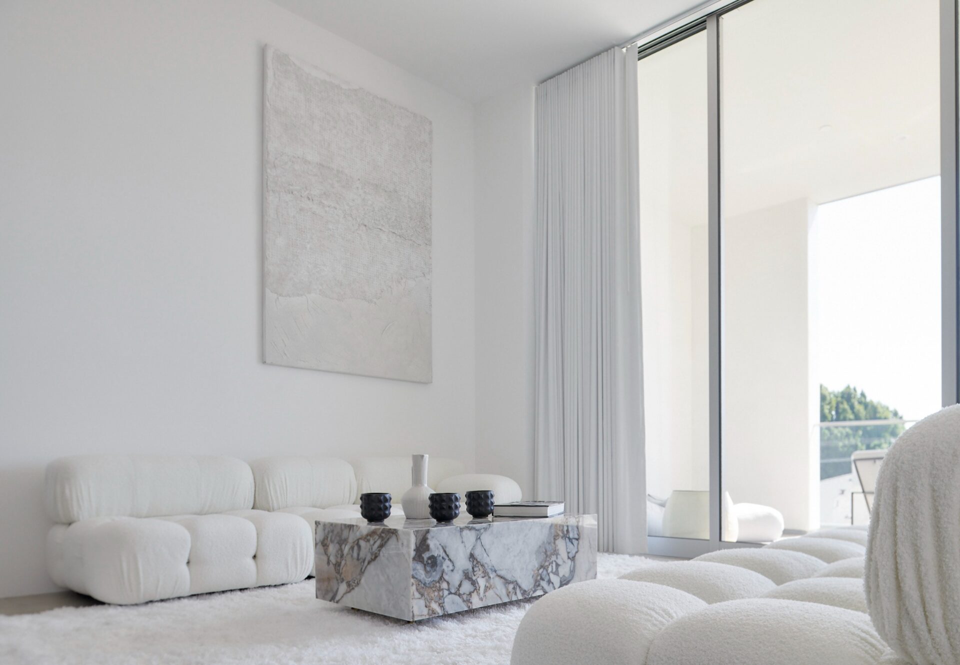 Monochrome penthouse living room with modular cream sofa, marble coffee table, and sliding glass doors opening to a private terrace.