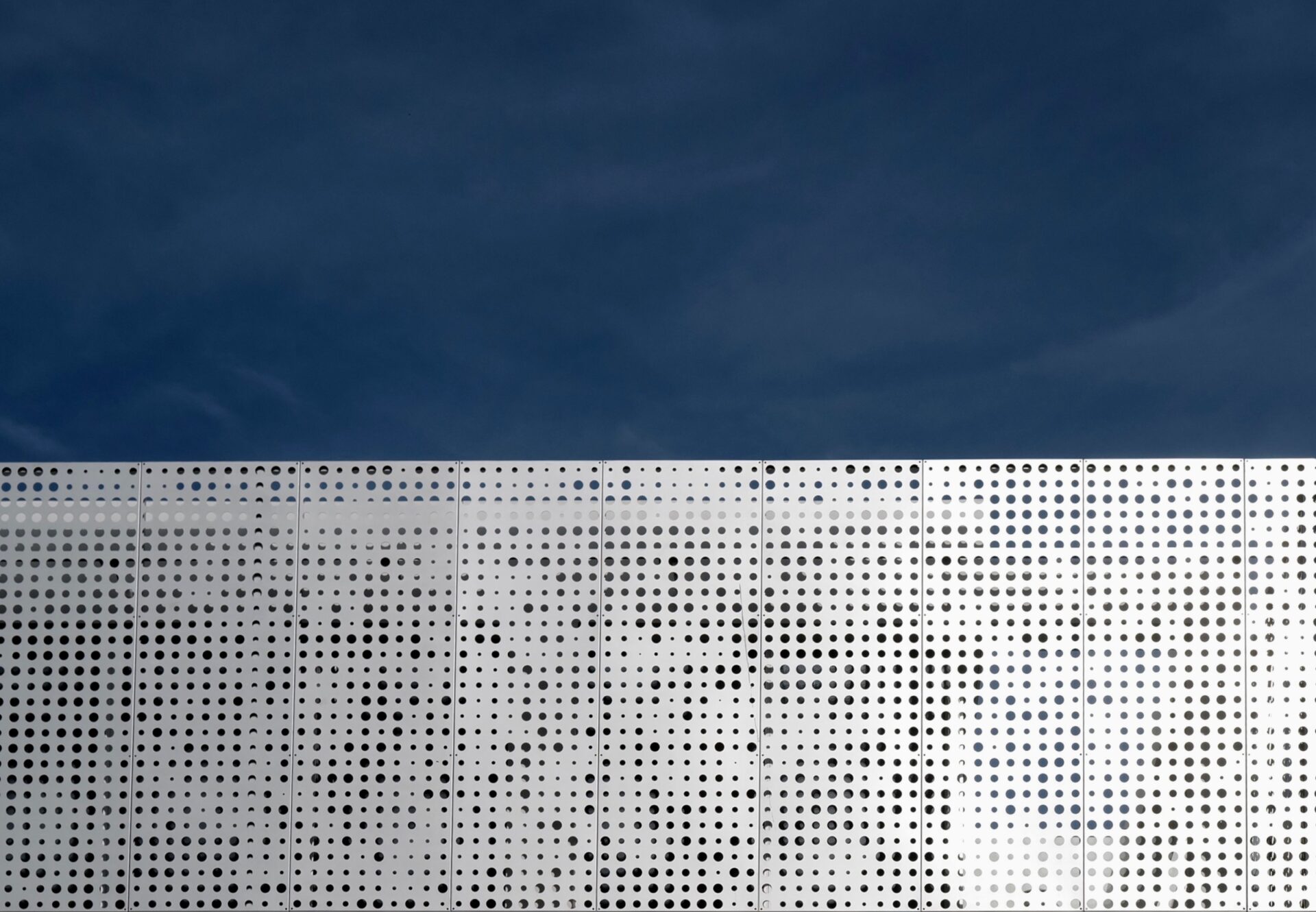 Perforated metal building facade under a deep blue sky, showcasing modern industrial design.
