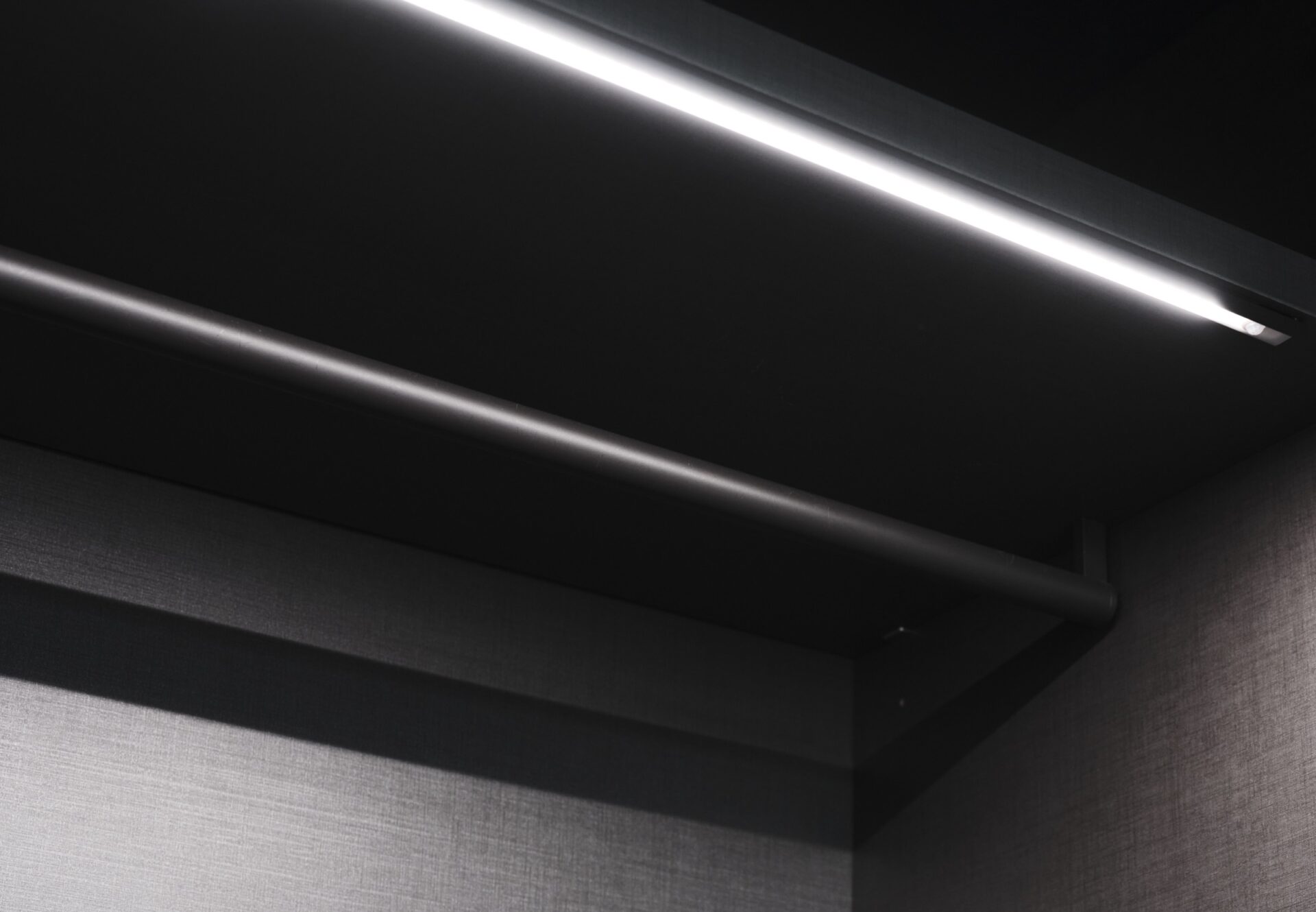 Recessed LED lighting strip above matte black closet rod.