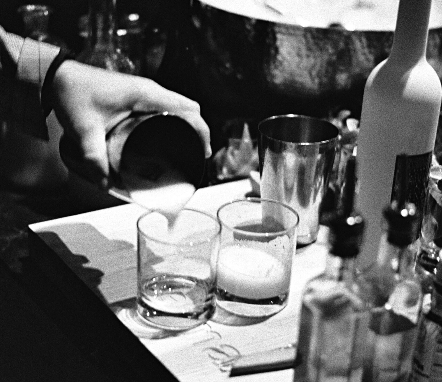 Close-up of a bartender pouring cocktails into glasses during an evening resident event on the rooftop terrace.