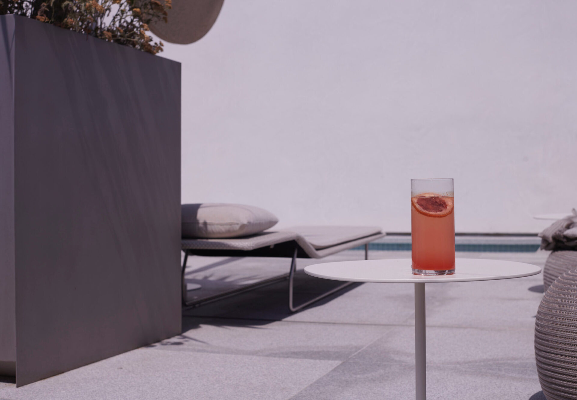 Rooftop sundeck with grapefruit cocktail on a white table, poolside loungers, and soft afternoon light.