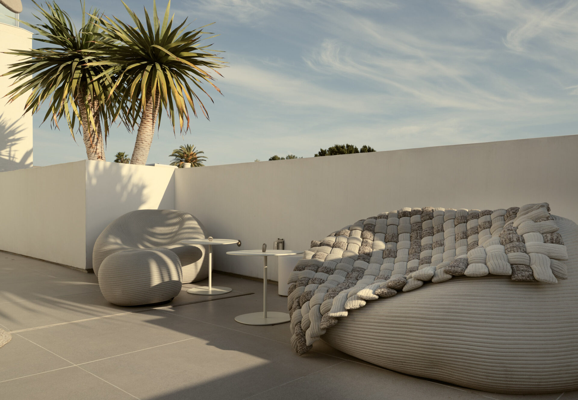 Rooftop sundeck lounge with Paola Lenti outdoor furniture, bathed in soft afternoon light beneath palm trees.