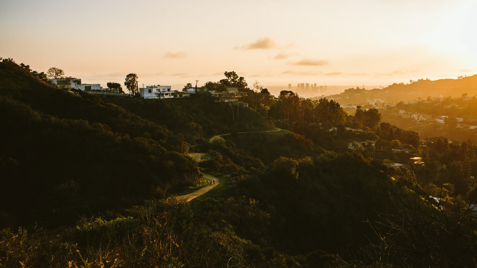 Sunset view over Runyon Canyon hills with picturesque houses and a winding path through lush greenery.