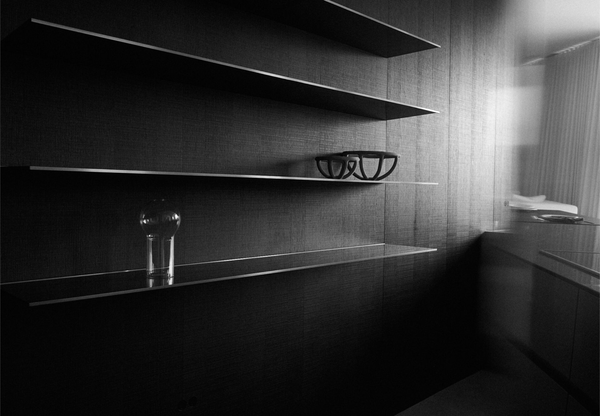 Open shelving with glassware and sculptural bowl, set against a textured wall in a minimalist kitchen space.