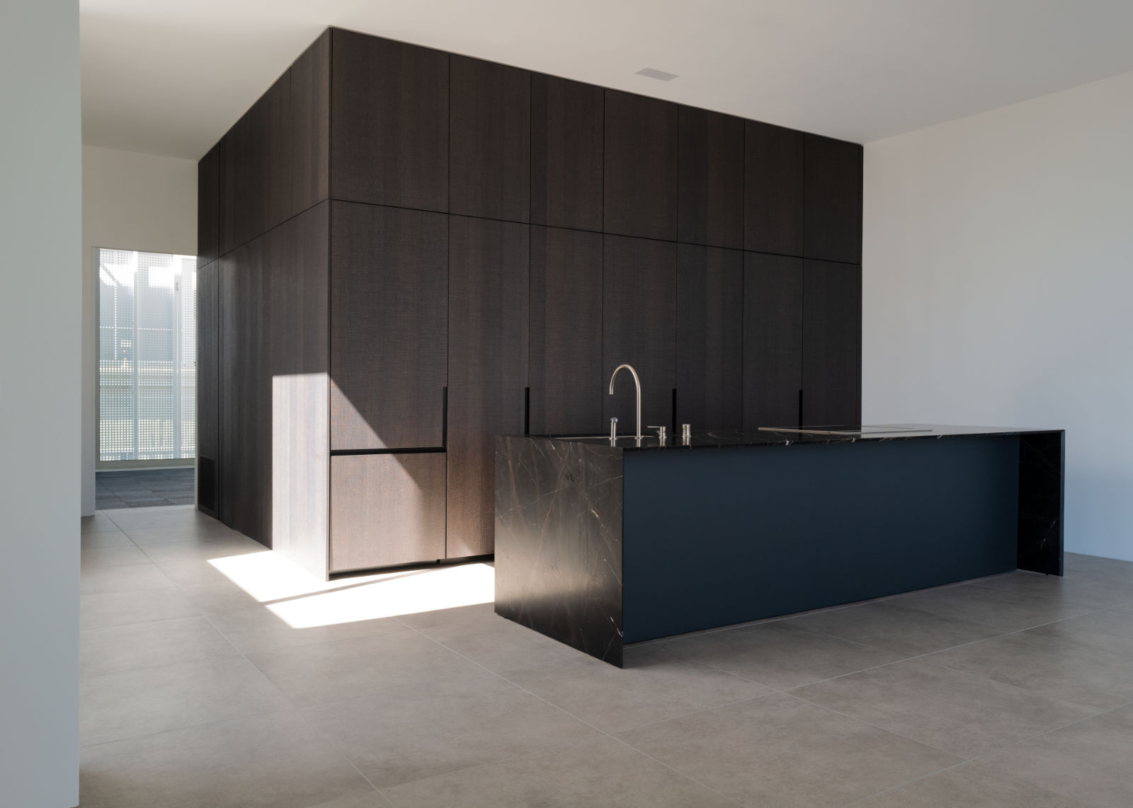 Spacious kitchen with floor-to-ceiling dark oak cabinetry and black marble island with integrated sink, illuminated by natural light.