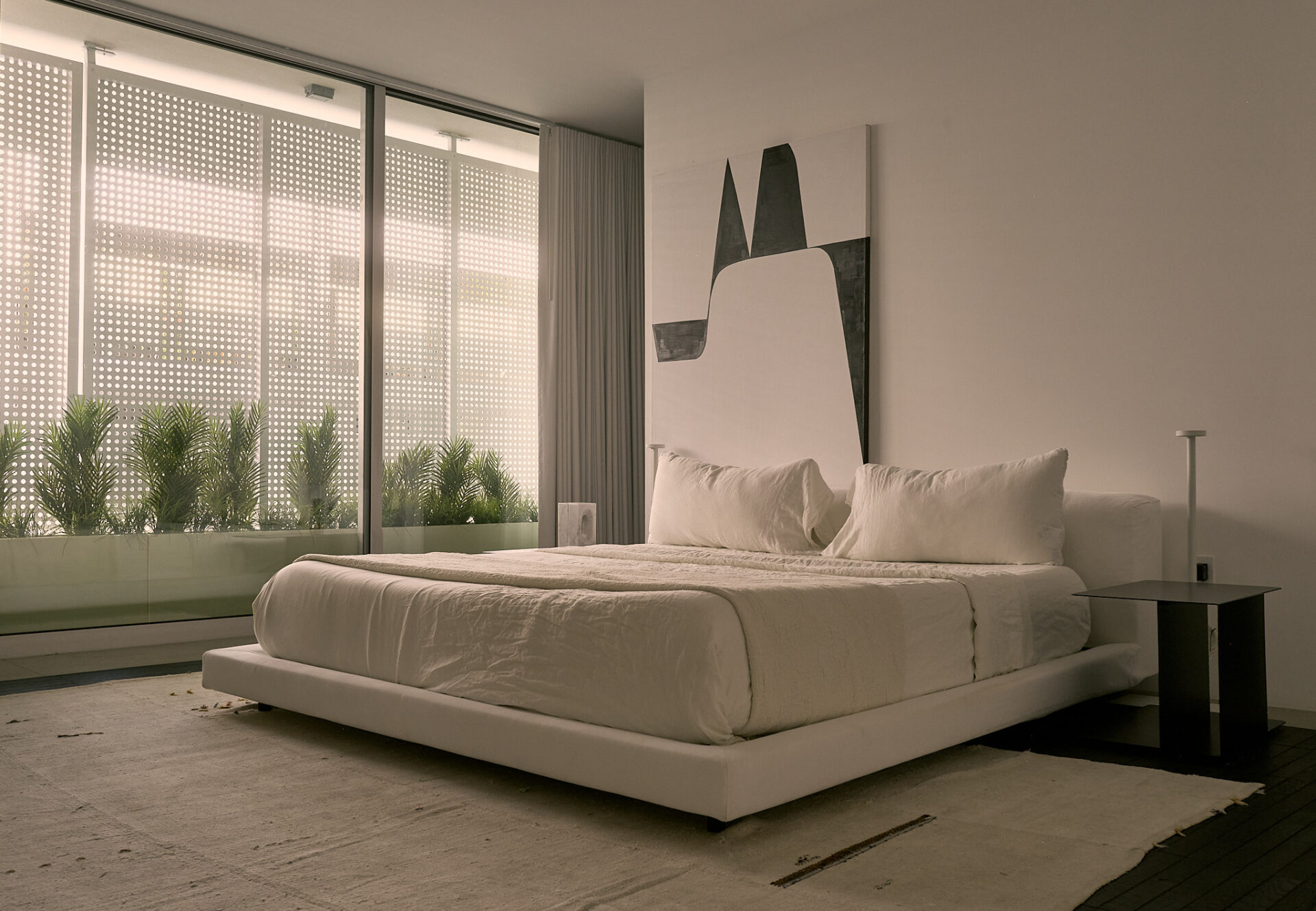 Primary bedroom with low-profile bed, abstract art, and sliding glass doors opening to a perforated veil privacy screen.
