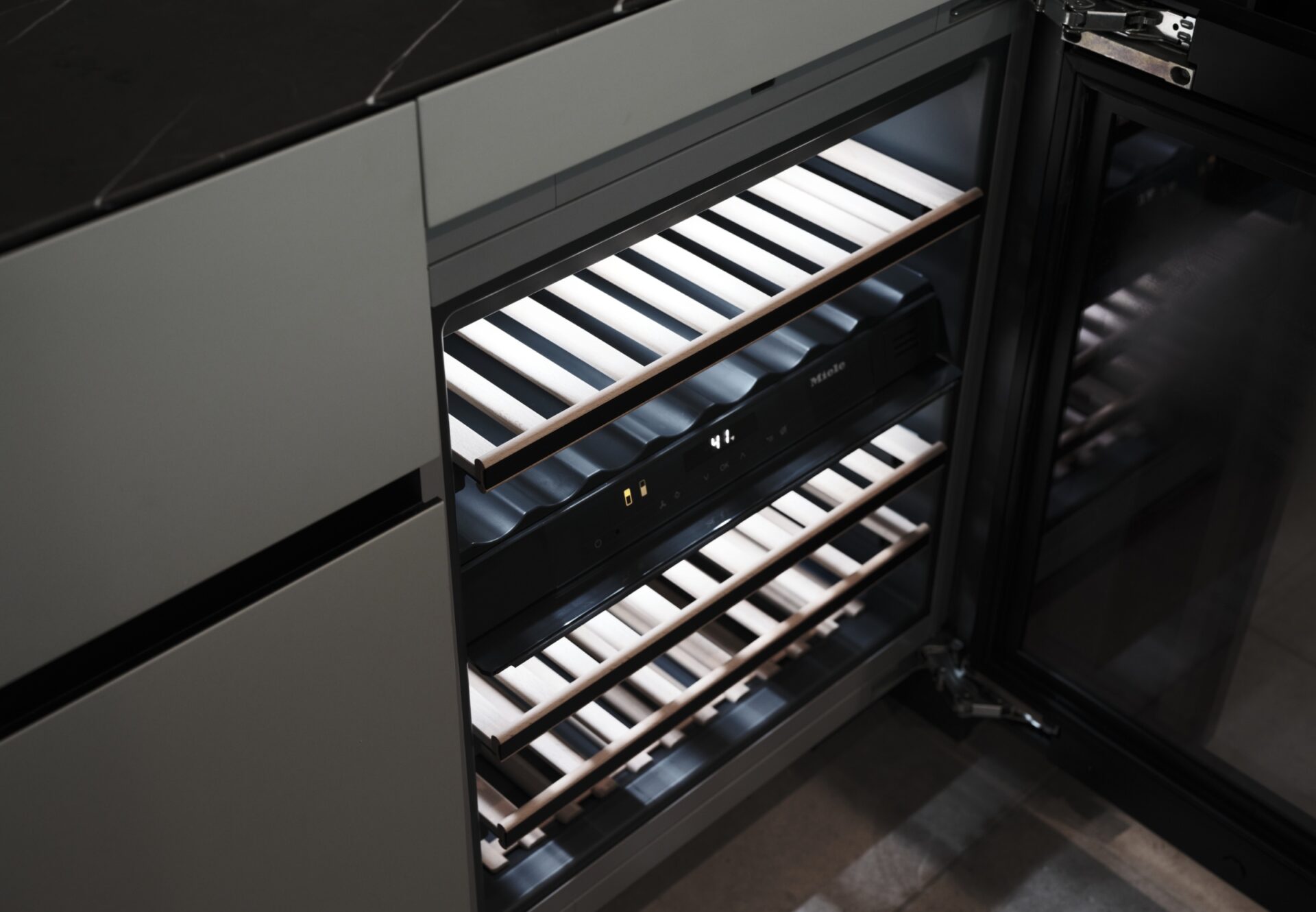 Built-in under-counter wine refrigerator with wooden shelves, integrated seamlessly into the modern kitchen cabinetry.