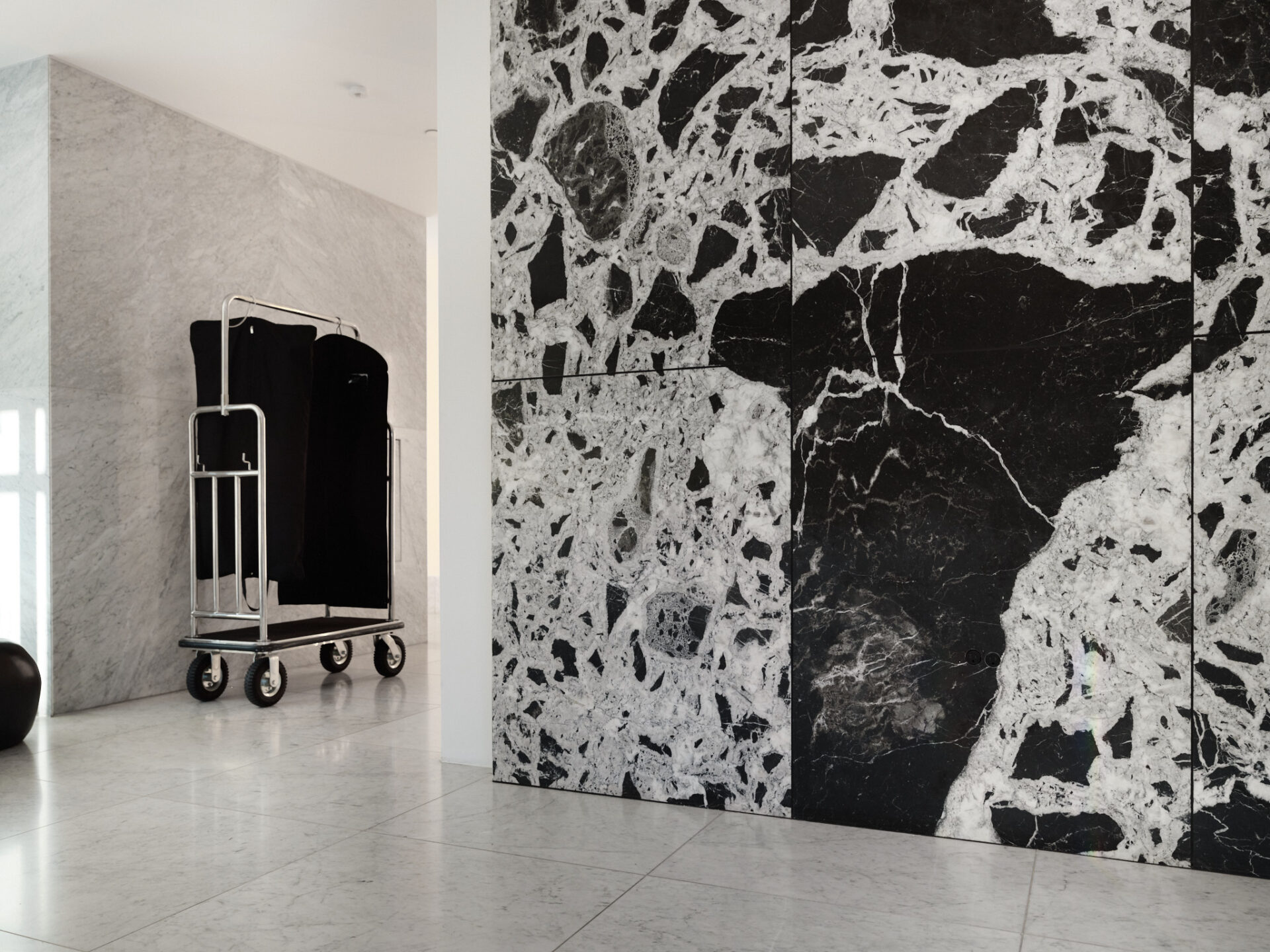 Concierge lobby featuring dramatic marble walls, polished stone floors, and garment cart with black linen covers.